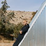 A person with medium skin lays back on a slanted metal roof, arms crossed.