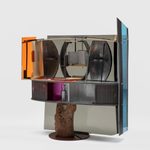 A multi-piece silver cabinet with colorful pops of orange, pink and blue on the sides and back. It balances on a wooden stump.
