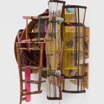 Rounded, wall mounted shelf made of wicker chairs and wrapped in clear vinyl.