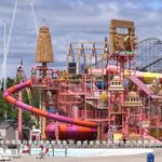 A photo of an entire outdoor waterpark, in bright colored in pink, yellow and orange. There are roller coasters and swing rides in the background.