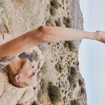 A person with medium skin lays back on a rock with their left hand raised in front of them.