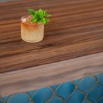 a iced beverage with orange and brown fluid with a copper straw and mint atop a wood and blue tiled bar top