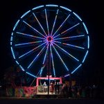 Ferris wheel outside at night, covered in colorful lights with a platform of guests standing in line for the ride