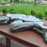 A bronze figure lays flat on a bench outside.