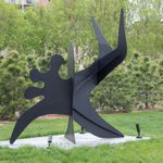 A metal sculpture with pointed, abstract edges sits in a grassy lawn.