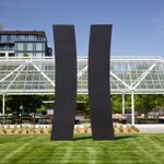 Two large, curved identical black sculptures stand upright on a grassy lawn