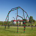 A green, black and red spider-like sculpture sits on a grassy lawn.