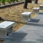 Five marble bench like structures with words engraved on top sit along side a sidewalk outside.