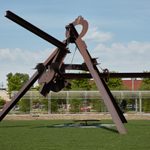 A large, angular sculpture made of metal sits on a grassy lawn outside.