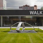 A large silver metal "X" sits horizontally on a concrete slab outside the Walker on a grassy lawn.