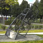 A metal sculpture, made up of several grid-like plates of black metal sits outside in a garden area.
