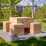A sculpture made of four box-like pieces sit on top of a concrete floor outside in a garden surrounded by trees.