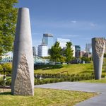 Tall concrete sculptures stand upright in a garden with a city in the background