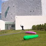 Green and pink oblong objects sit on a green lawn outside a modern building.