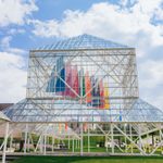 A large glass building in an outdoor space with white metal structures holding it up.
