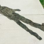 Concrete sidewalk with a faint image of a person etched into the cement. Green grass pathway surrounds the sidewalk and figure.