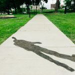 Concrete sidewalk with a faint image of a person etched into the cement. Green grass pathway surrounds the sidewalk and figure.