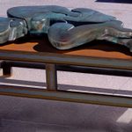 A bronze figure lays flat on a bench outside.