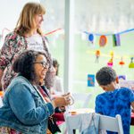 Two adults smile at a child working on an art project. 