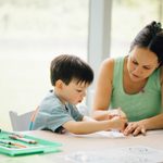 Adult holds tracing paper down on table while child traces a design with a marker.